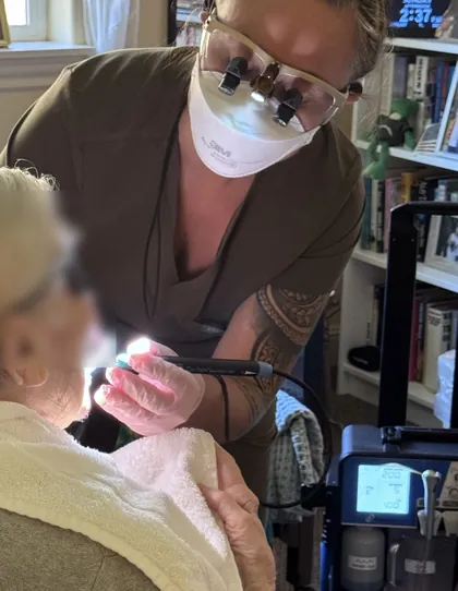 Jennifer cleaning an older patient’s teeth where they are sitting